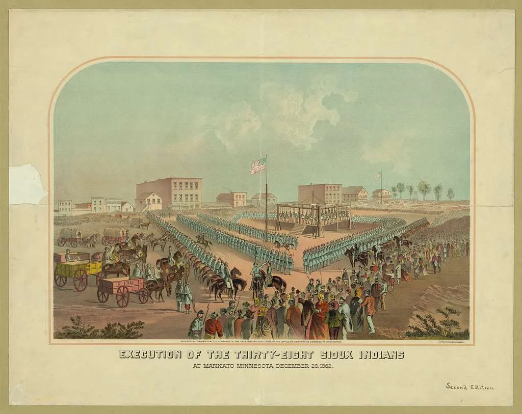 A print shows a massive gallows with Mankato buildings in the background. The gallows faces an American flag, and is surrounded on three sides by soldiers, with many public onlookers beyond them