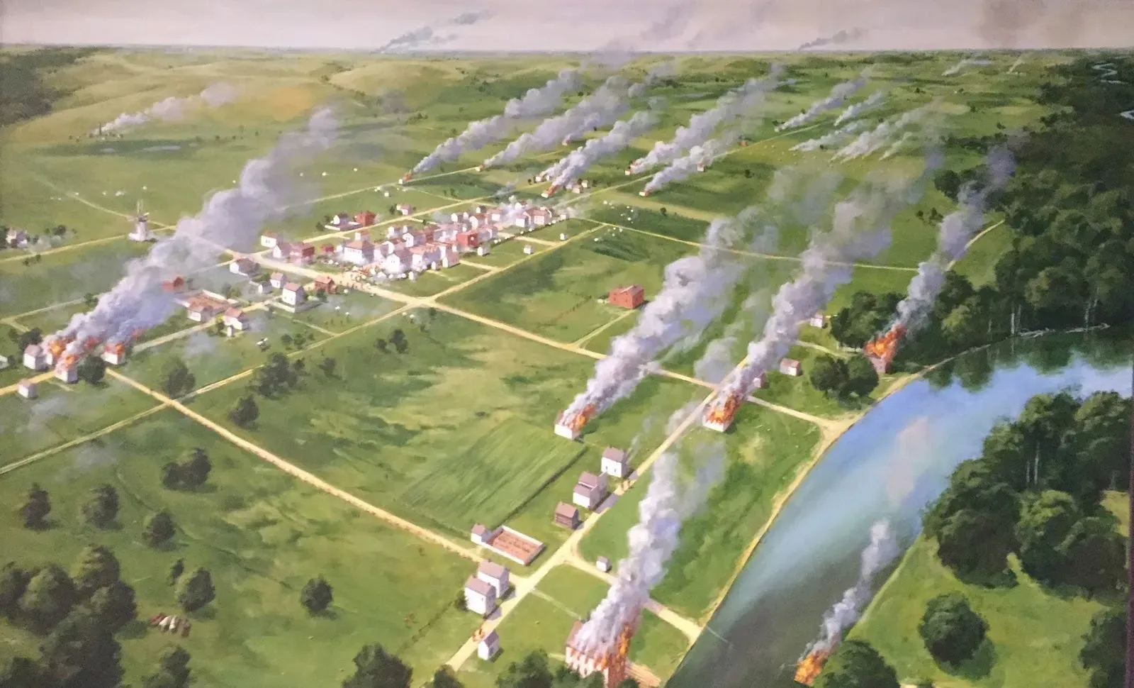 Aerial view of New Ulm, a simple collection of buildings, clustered around a main street, with many building on fire